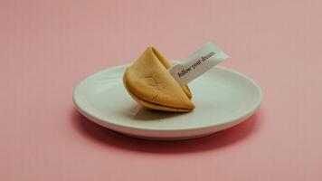 A fortune cookie on a white plate with a message that says follow your dreams on a pink background photo