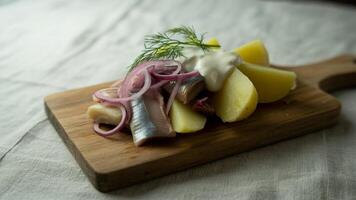 Herring salad with potatoes red onions dill and sour cream on a wooden cutting board close up view photo