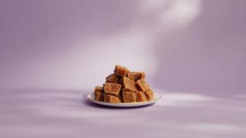 A stack of caramel fudge pieces on a small plate against a light purple background in soft studio light photo