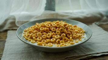 A bowl of breakfast cereal rings with milk on a linen cloth near a window with white curtains photo