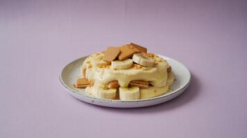 A plate of banana pudding with wafers and sliced bananas on a light purple colored background photo