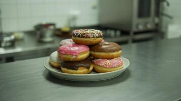 A stack of delicious donuts with various toppings on a plate in a kitchen setting with metal counter photo