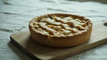 A close up of a lattice topped peach pie on a wooden board with a textured white tablecloth background photo