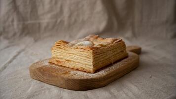 Close up of a mille feuille pastry dusted with sugar on a wooden board with a textured background photo