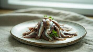 A pile of anchovies on a plate garnished with parsley sitting on a linen cloth with a window behind photo