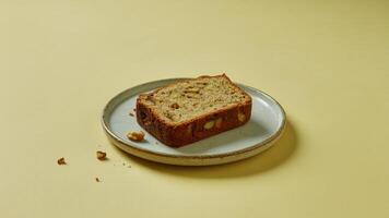 A slice of banana nut bread on a round plate against a yellow background in a studio setting photo