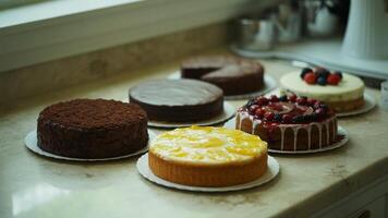 A collection of various cakes displayed on a countertop in a kitchen setting with natural lighting photo