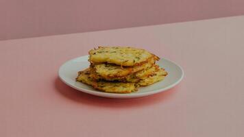 Stack of potato pancakes with herbs on a white plate against a pink background in a studio setting photo
