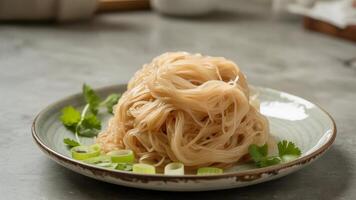 a bowl of noodles with vegeta bles a nd chopsticks resting on the rim on a wooden surfa ce nea r a wa ll photo