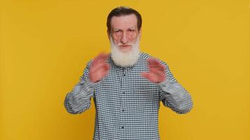 I will not say anything. Frightened senior man closing mouth with hands, looking intimidated scared at camera gestures no refusing to tell secret unbelievable truth. Grandfather on yellow background video