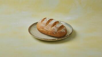 a loa f of golden brown brea d sitting on a white pla te a ga inst a yellow ba ckground in a studio setting photo