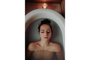 A woman relaxing in a bathtub with her eyes closed and a candle burning above her photo