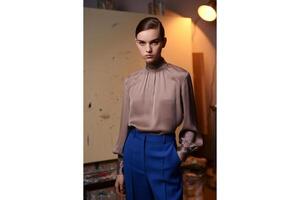 Woman in blouse and blue pants poses in front of a canvas in an art studio space photo