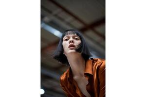 Portrait of a woman with a bob haircut and orange shirt looking up at the camera photo