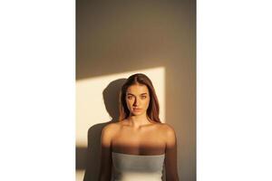 Portrait of a woman with brown hair and green eyes in sunlight against a wall photo