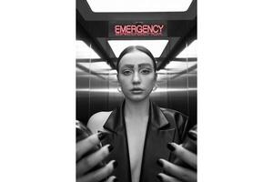 Woman with unique eyebrows in elevator under emergency sign in black and white photo