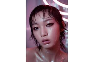 Close up of a woman with wet hair and dramatic eyeliner in a pink lit setting photo