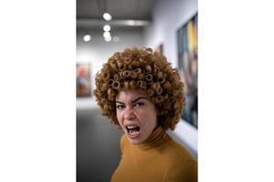 A woman with curly hair and mustard turtleneck making an angry expression at viewer photo