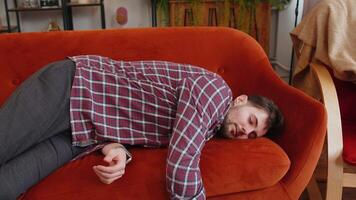 Exhausted young man in plaid shirt flopped down on sofa falls asleep. Concept of after party, tired overworked person hard day, lack of energy, breakdown. Caucasian drunk bored guy sleeping on couch. video