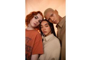 Three diverse models posing closely together in front of a peach colored backdrop photo