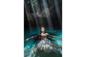 Woman in white dress floating in turquoise water with sunlight streaming down above photo