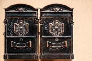 Vintage-style metal mailboxes mounted on a wall. Each box features ornate decorations with a crest. photo