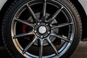 A close-up of an alloy car wheel featuring a multi-spoke design. The metallic spokes have a dark, polished finish, contrasting with the silver center cap. photo
