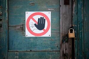 Weathered wooden door with peeling turquoise paint. Caution sign a black hand symbol inside a red circle with a diagonal line, indicating prohibition photo