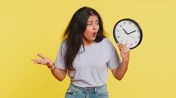 Indian young woman with anxiety checking time on clock, running late to work, being in delay, deadline. Arabian girl looking at hour, minutes, worrying to be punctual isolated on yellow background video