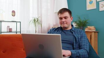 Happy Caucasian man sitting on sofa closing laptop and relaxing after finishing work in living room. Young guy freelancer works online remote job at home. E-learning, browsing internet on netbook. video