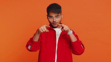 I am watching you. Confident attentive man pointing at his eyes and camera, show I am watching you gesture spying on someone. Handsome disappointed Indian guy isolated on orange studio background video