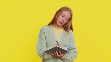 Thoughtful journalist Caucasian middle-aged woman 40 years old making notes, writing down thoughts with pen into notepad notebook diary, to do list, good idea. Adult girl isolated on yellow background video