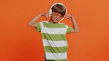 Happy smiling preteen child boy in headphones listening music dancing disco fooling around having fun expressive gesticulating hands relaxing on party making funny moves. Kid on orange background video