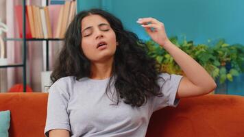Sick ill Indian woman rubbing temples to cure headache problem, suffering from tension and migraine, stress, grimacing in pain, high blood pressure at home. Arabian girl indoors in room on couch video
