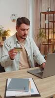 Happy Caucasian man freelancer using bank credit card and laptop for online shopping payments at home office. Business transaction. Smiling guy purchase with computer E-banking app service. Vertical. video