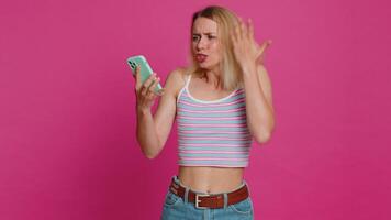 Upset sad Caucasian woman use smartphone typing browsing, play game, loses, surprised by sudden lottery results bad fortune loss fail unlucky news. Pretty beautiful girl isolated on pink background video