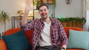 Portrait of cheerful young man in plaid shirt smiling at camera and waving gesturing hello, hi, greeting or goodbye. Happy Caucasian guy making webcam conference call with friend at home room video