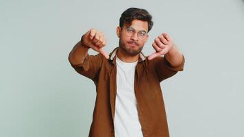 Dislike. Upset unhappy Indian man showing thumbs down sign gesture, expressing discontent, disapproval, dissatisfied negative feedback. Attractive bearded guy indoors isolated on gray background video