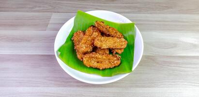 Crispy Thai fried bananas with sesame seeds served on a banana leaf in a white plate, Fried bananas is a traditional Asian snack with sweet, crunchy texture. Top view close-up shot, copy space photo