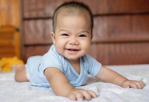Happy Asian baby girl smiling and lying on his stomach on a bed at home, showing first teeth. Concept of childhood, innocence, and happiness photo