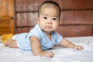 Happy Asian baby girl smiling and lying on his stomach on a bed at home, showing first teeth. Concept of a childhood, innocence, and happiness photo