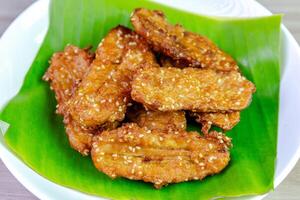 Crispy Thai fried bananas with sesame seeds served on a banana leaf in a white plate, Fried bananas is a traditional Asian snack with sweet, crunchy texture. Top view close-up shot photo