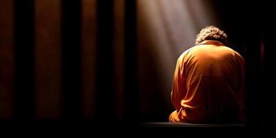 Prisoner in Orange Jumpsuit Sitting Alone in Cell Back View Dark Penitentiary Setting photo