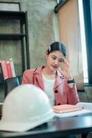 Young woman in office, focused on work with construction helmet and documents, representing professional and engineering themes. photo