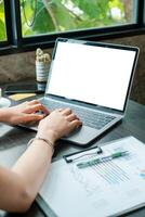 Hands typing on a laptop with a blank screen, surrounded by documents and greenery in a bright office. photo