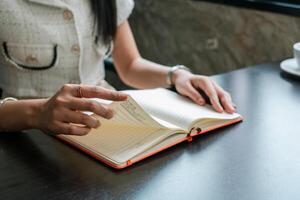 Close-up of a woman turning pages in a notebook at a cafe, capturing a moment of relaxation and focus. photo