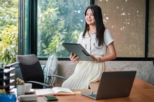 A young woman using a tablet in a bright, modern office setting, surrounded by greenery and natural light. photo