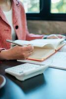 A business professional takes notes in a planner with a calculator on the desk, capturing a moment of productivity in a modern office. photo