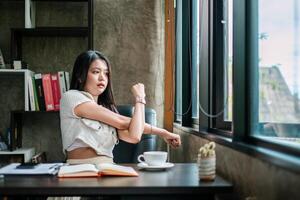 Young woman stretches at her desk, enjoying a break with coffee and an open notebook in a modern office setting. photo