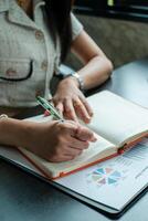 Professional woman taking notes in a notebook with financial charts on a desk, showcasing business and finance concepts. photo